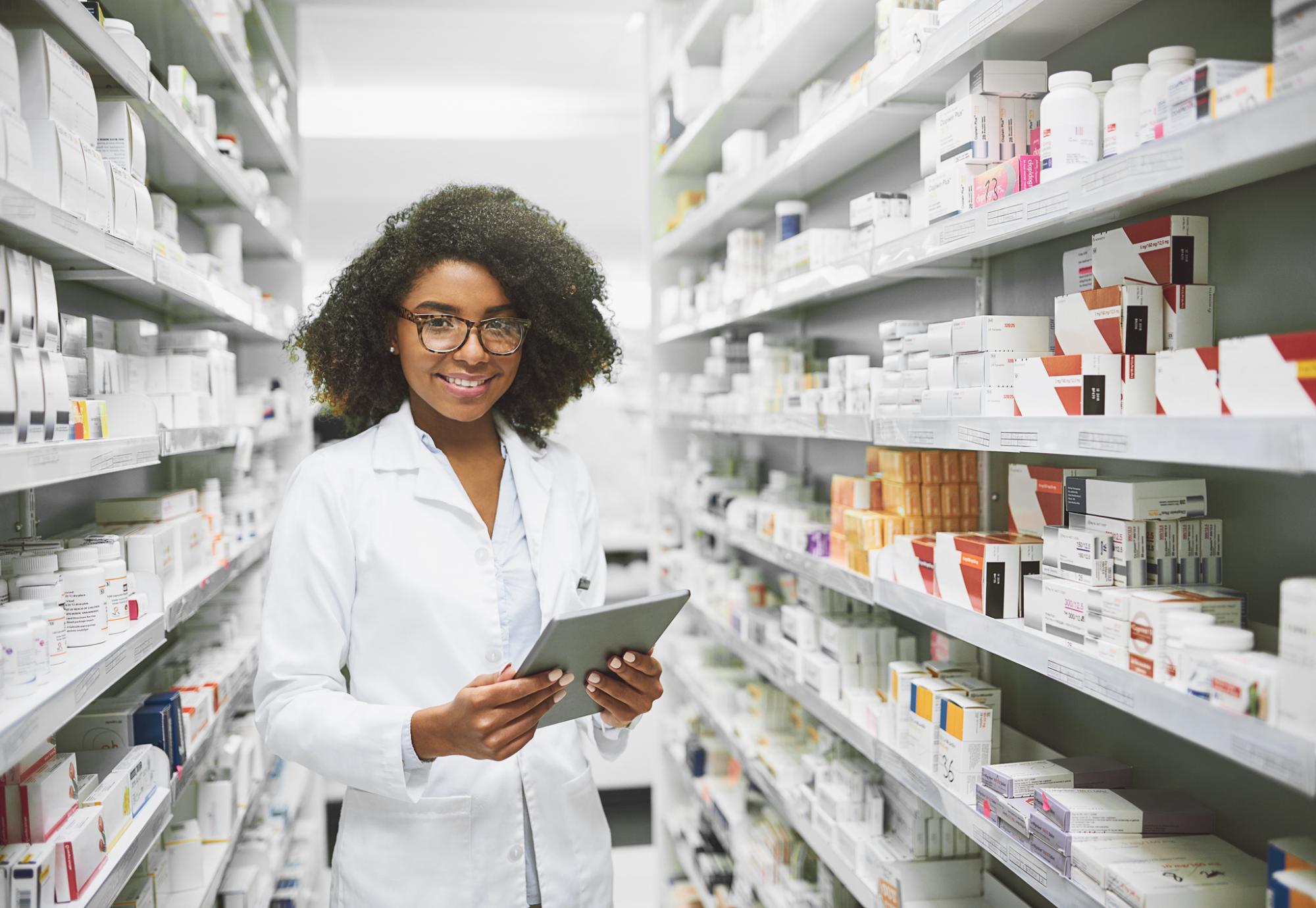 Female doctor holding a tablet and smiling in the pharmacy.